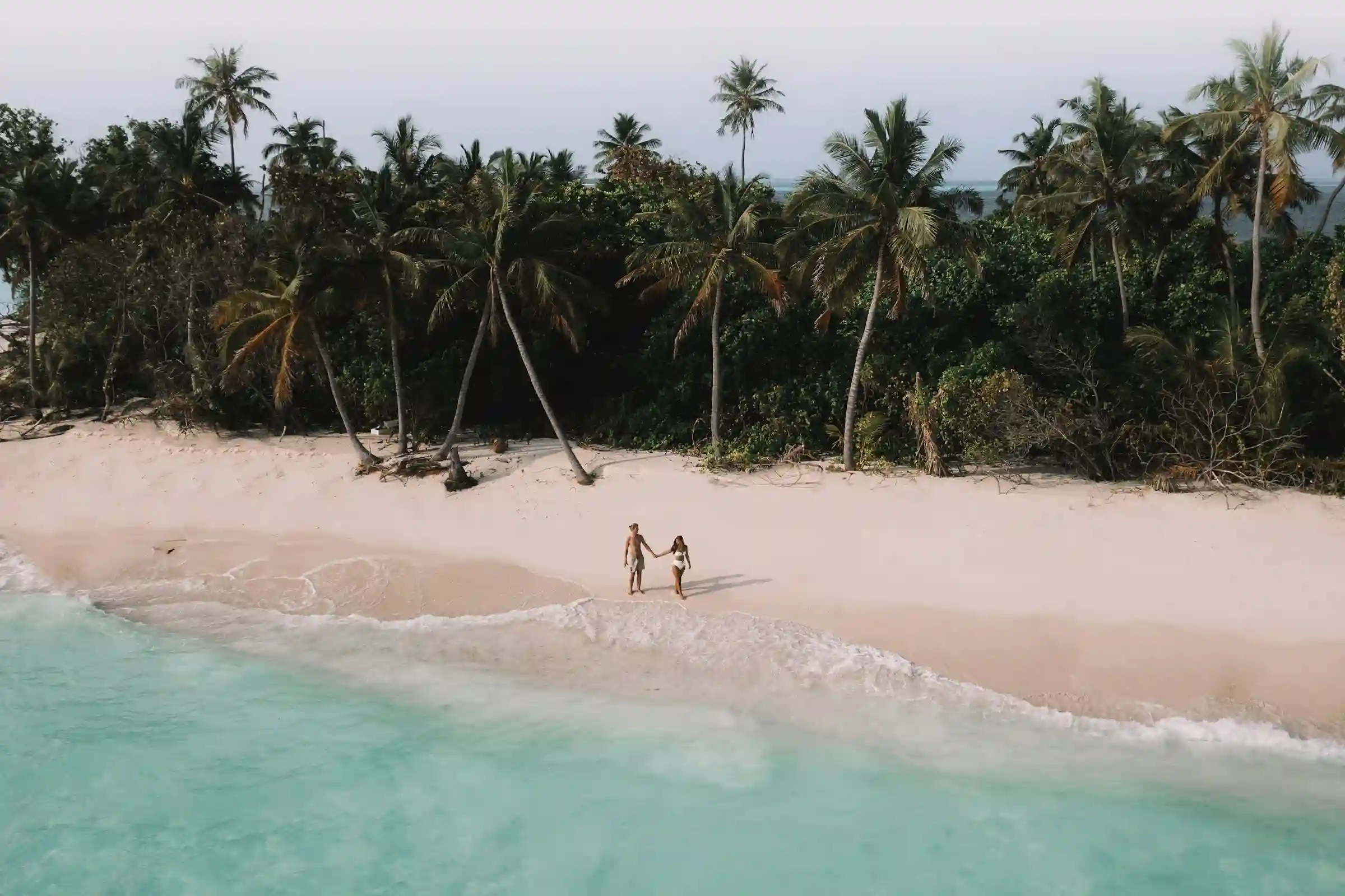 Pareja caminando de la mano frente a un atardecer cálido, representando la curaduría de experiencias románticas y el diseño de viajes para parejas de True Ventour.