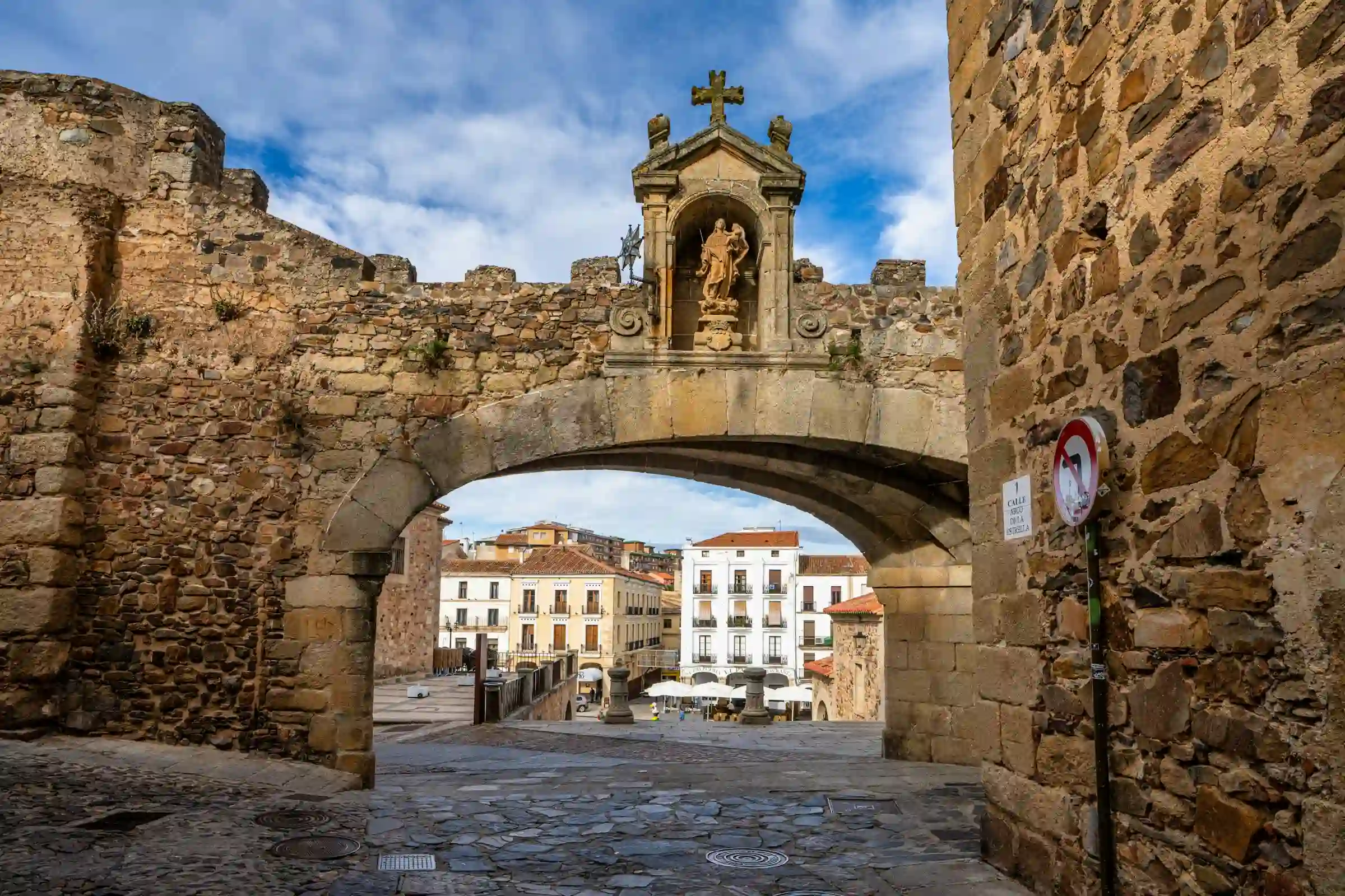 Vista de un arco de piedra histórico con una estatua religiosa en un entorno urbano antiguo, representando la profundidad cultural y la gestión impecable de los viajes de fe de True Ventour.