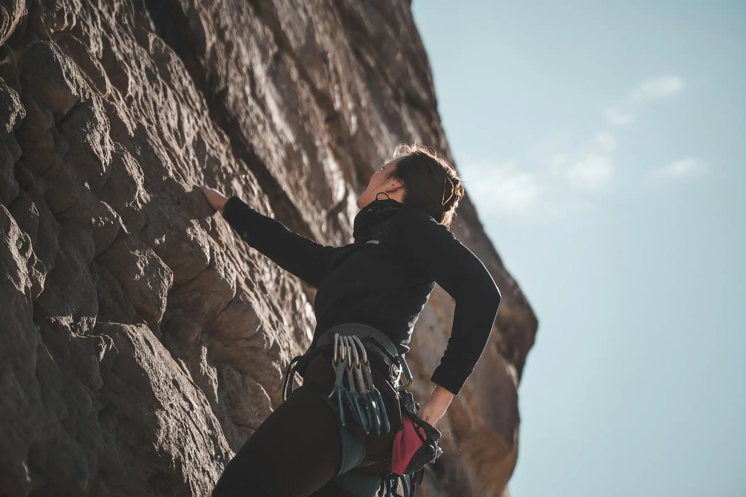 Una escaladora en una pared de roca vertical, representando el desafío personal y la precisión técnica en la logística de viajes deportivos de True Ventour.