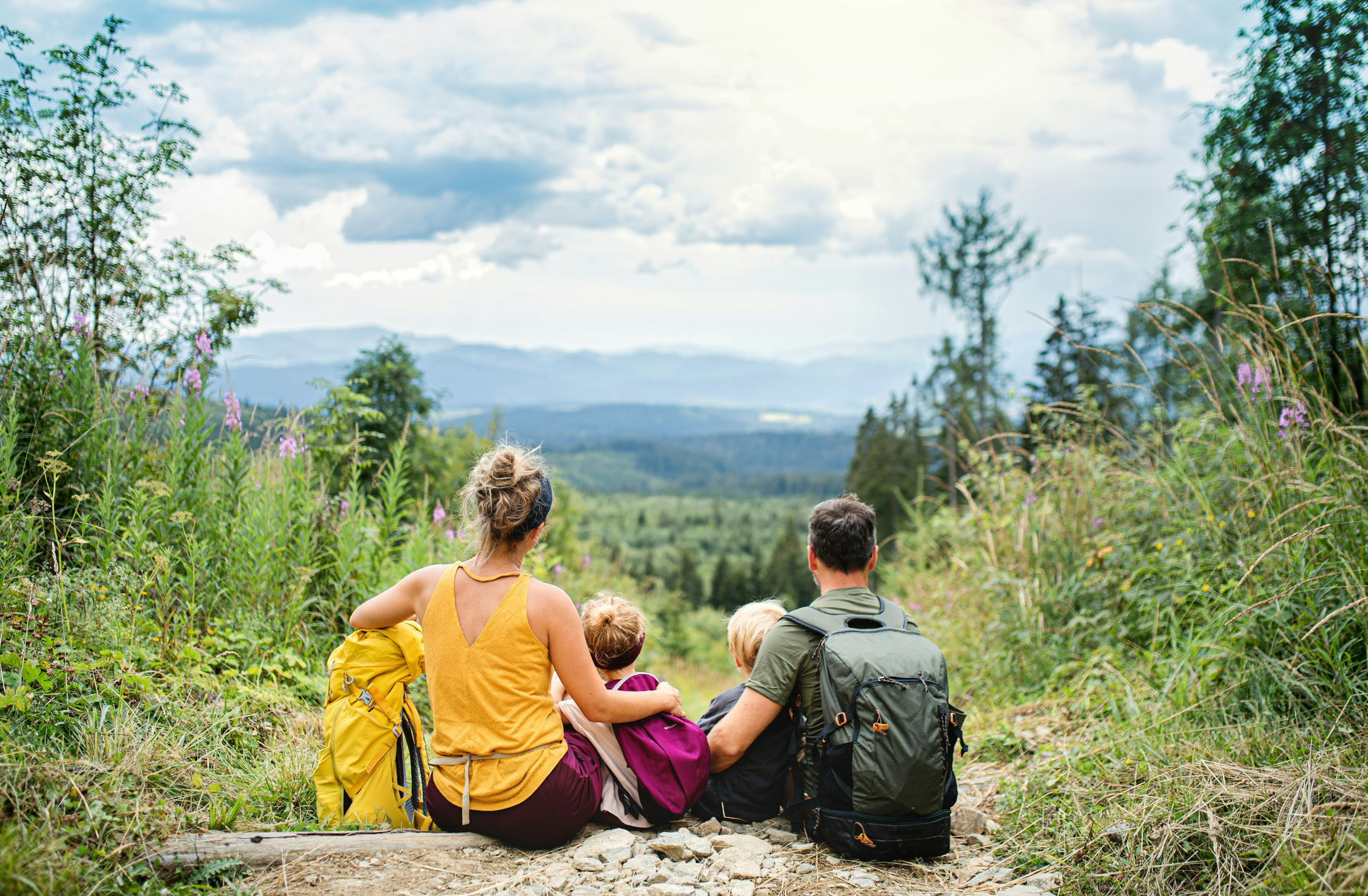 Familia con mochilas sentada en un sendero de montaña contemplando el paisaje, representando viajes familiares a medida y eventos de grupo con propósito.